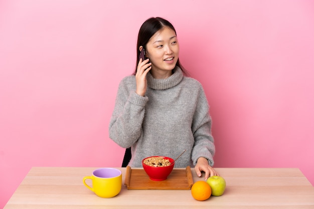 Giovane donna cinese facendo colazione in un tavolo mantenendo una conversazione con il telefono cellulare