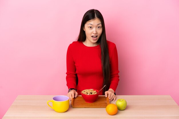 Young Chinese woman having breakfast in a table with surprise facial expression