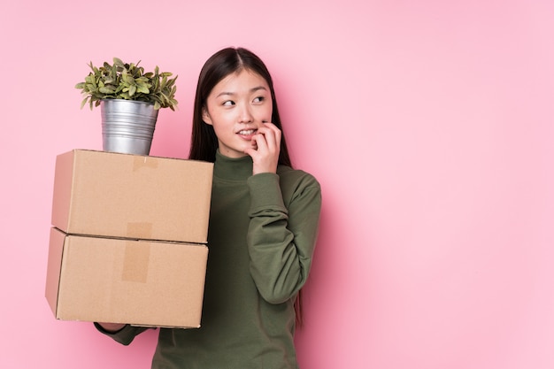 Young chinese woman holding boxes relaxed thinking about something looking at a blank space.