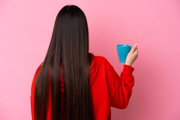 Young chinese woman holding cup of coffee isolated on pink background in back position