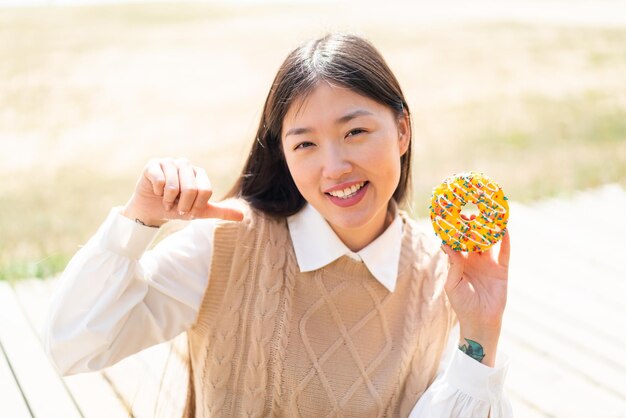 야외에서 자랑스럽고 자기 만족스러운 도넛을 들고 있는 젊은 중국 여성