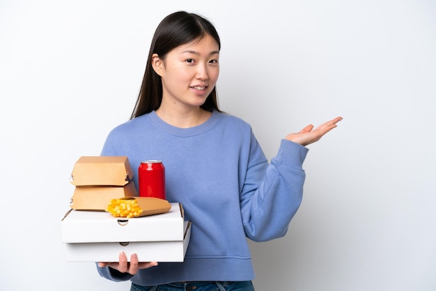 흰색 배경에 격리된 패스트 푸드를 들고 오는 젊은 중국 여성이 손을 옆으로 내밀어 초대합니다