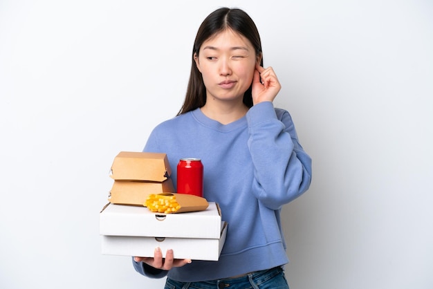 흰색 배경에 격리된 패스트푸드를 들고 좌절하고 귀를 덮는 젊은 중국 여성