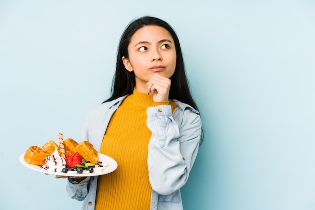 青い壁に分離された食品皿を保持している若い中国人女性