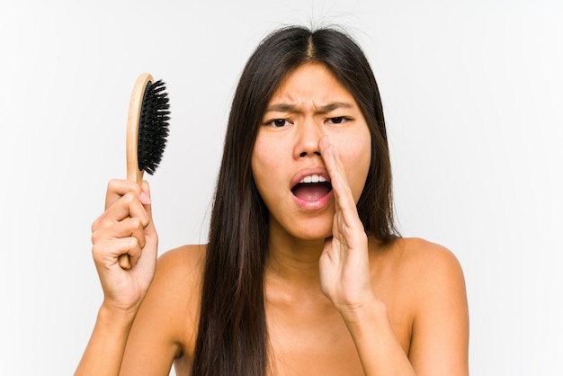 Young chinese woman holding a hairbrush isolated shouting excited to front.