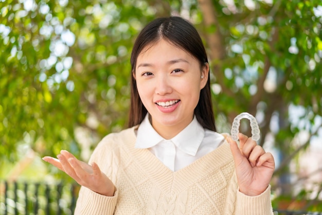 충격을 받은 표정으로 야외에서 보이지 않는 중괄호를 들고 있는 젊은 중국 여성