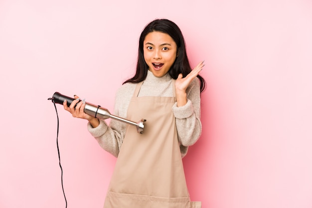 Young chinese woman holding a mixer isolated screaming very angry and aggressive.