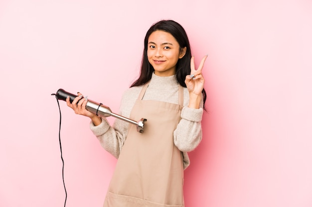 Young chinese woman holding a mixer isolated with fingers on lips keeping a secret.