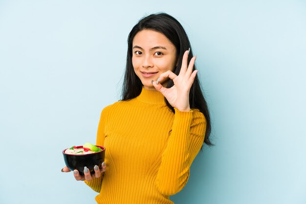 Young chinese woman holding noodles showing fist to camera, aggressive facial expression.