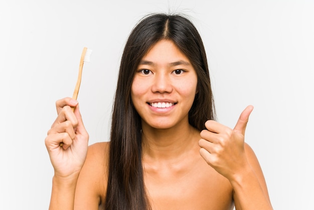 Young chinese woman holding a teeth brush isolated smiling and raising thumb up