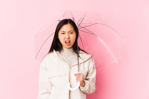 Young chinese woman holding a umbrella isolated screaming very angry and aggressive.