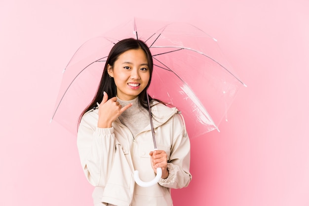 Young chinese woman holding a umbrella isolated showing a mobile phone call gesture with fingers.