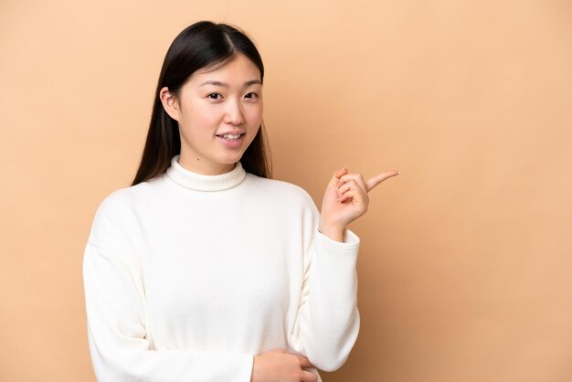 側に指を指しているベージュ色の背景に分離された若い中国人女性