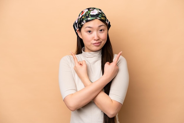 Young Chinese woman isolated on beige background pointing to the laterals having doubts