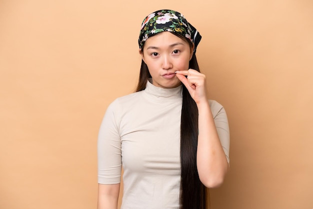 Young chinese woman isolated on beige background showing a sign
of silence gesture