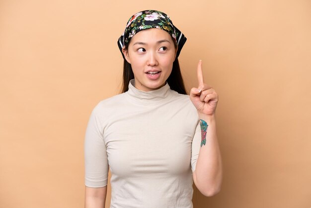 손가락을 가리키는 아이디어를 생각하는 베이지색 배경에 고립 된 젊은 중국 여성
