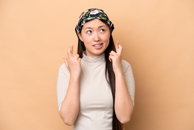 Young chinese woman isolated on beige background with fingers
crossing and wishing the best