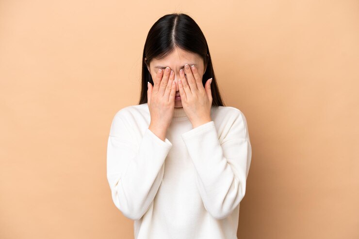 피곤하고 아픈 표정으로 베이지색 배경에 고립 된 젊은 중국 여자
