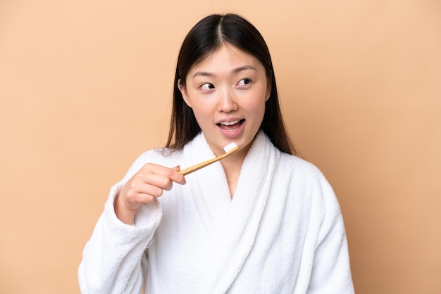 Young Chinese woman isolated on beige background with a toothbrush