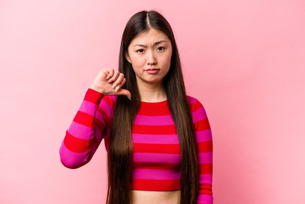Фото Молодая китаянка, изолированная на розовом фоне, показывает жест неприязни, опустив палец вниз