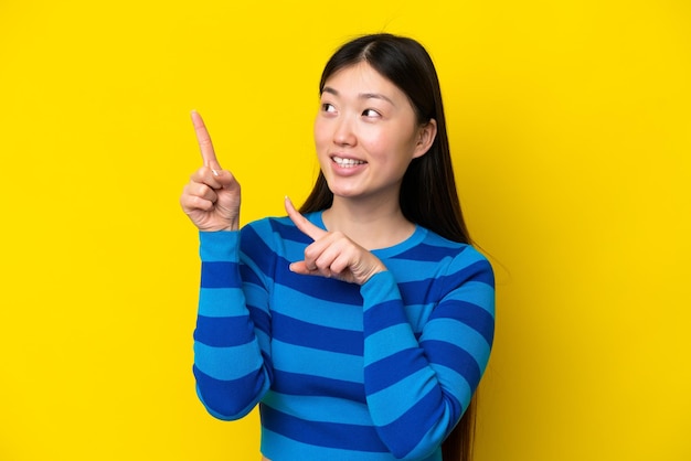 写真 人差し指で素晴らしいアイデアを指している黄色の背景に分離された若い中国人女性