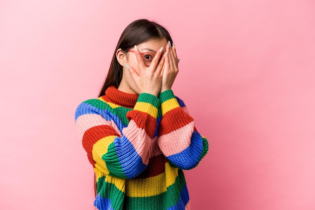 Young Chinese woman isolated on pink background blink through fingers frightened and nervous