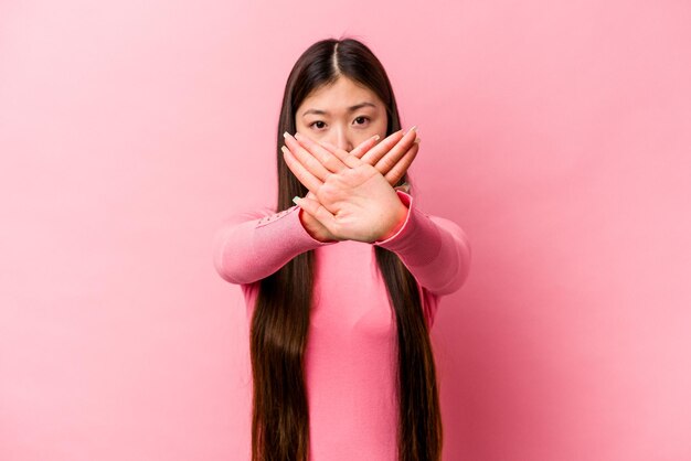 拒否ジェスチャーをしているピンクの背景に分離された若い中国人女性