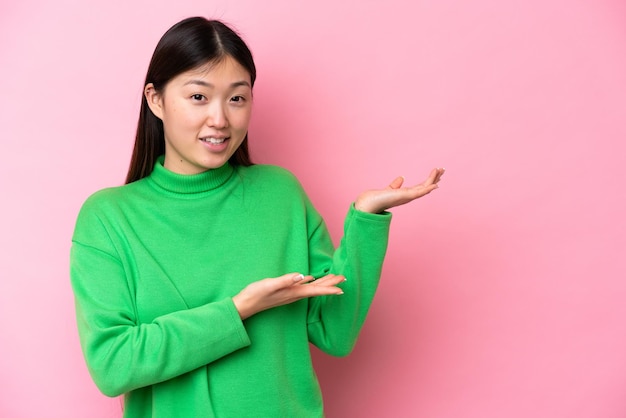 Young Chinese woman isolated on pink background extending hands to the side for inviting to come