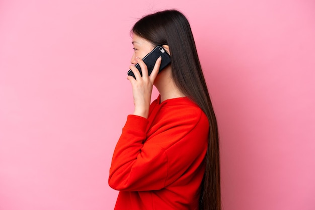 Young chinese woman isolated on pink background keeping a
conversation with the mobile phone with someone