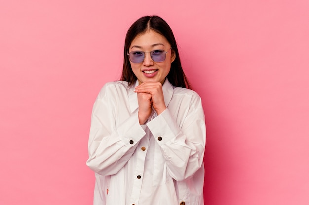 Young chinese woman isolated on pink background keeps hands under chin, is looking happily aside.