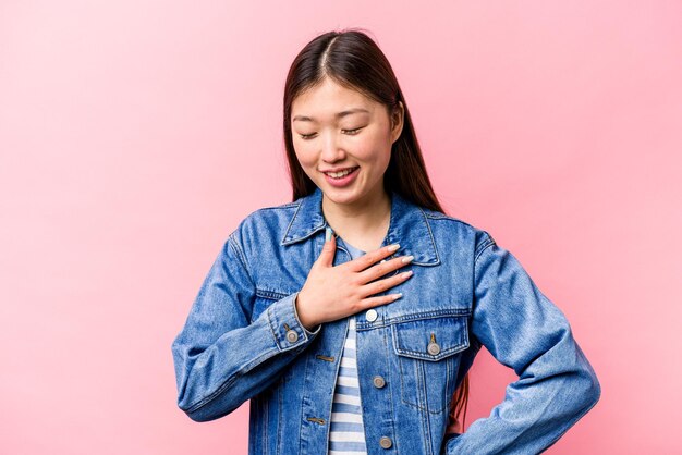 Young Chinese woman isolated on pink background laughing keeping hands on heart concept of happiness