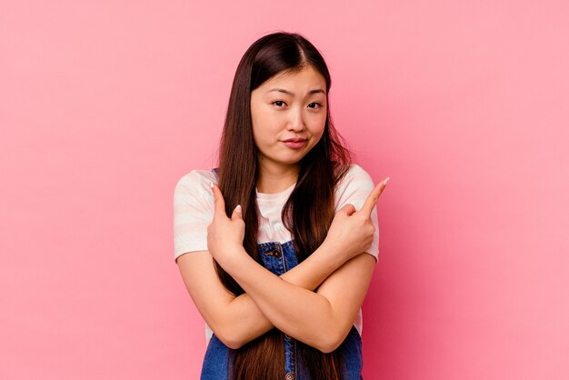 Young chinese woman isolated on pink background points sideways, is trying to choose between two options.