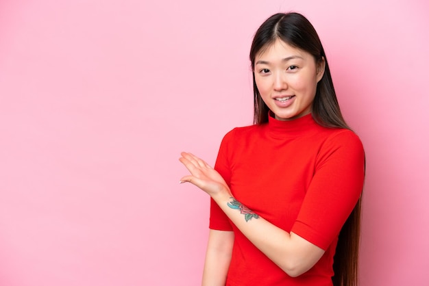 Young Chinese woman isolated on pink background presenting an idea while looking smiling towards