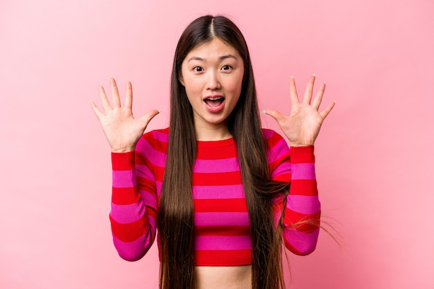 Young Chinese woman isolated on pink background receiving a pleasant surprise excited and raising hands