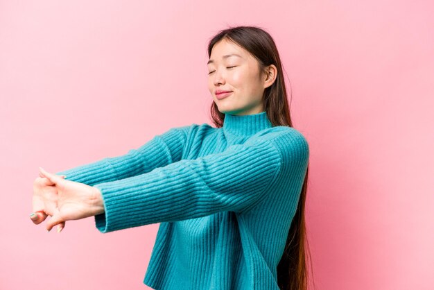 Молодая китаянка изолирована на розовом фоне, протягивая руки в расслабленном положении
