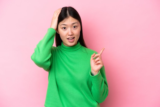 Young Chinese woman isolated on pink background surprised and pointing finger to the side