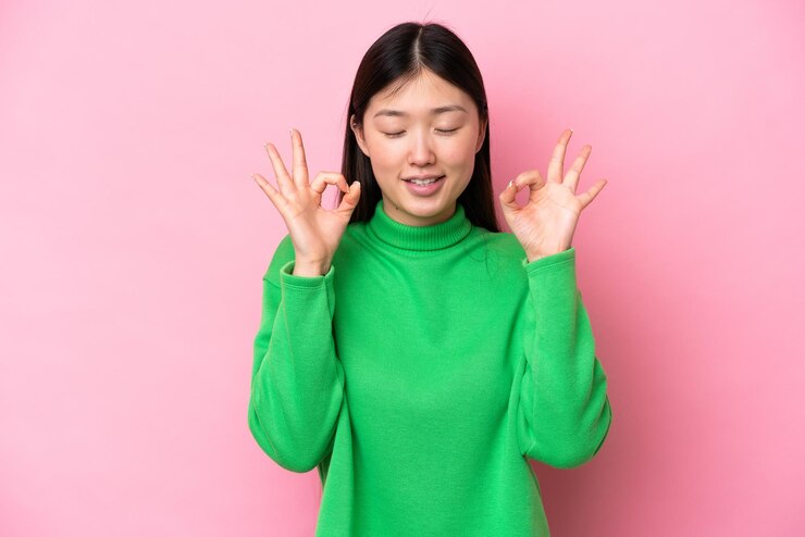 Photo 禅のポーズでピンクの背景に分離された若い中国人女性
