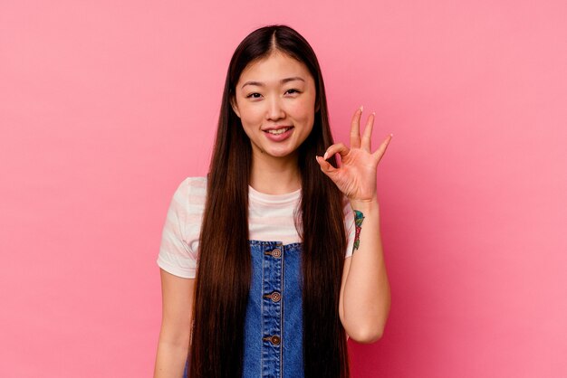 Young chinese woman isolated on pink wall cheerful and confident showing ok gesture.