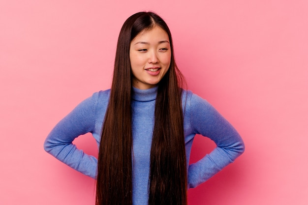 Young chinese woman isolated on pink wall confident keeping hands on hips.