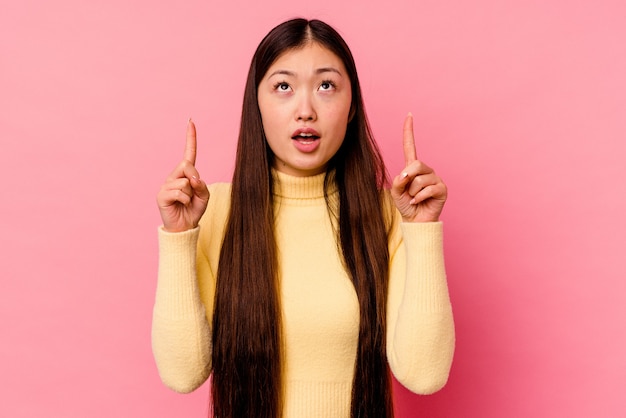 Young chinese woman isolated on pink wall pointing upside with opened mouth