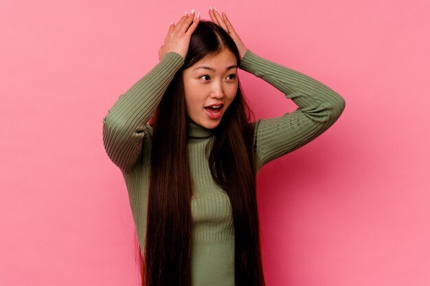 Young chinese woman isolated on pink wall screaming, very excited, passionate, satisfied with something.