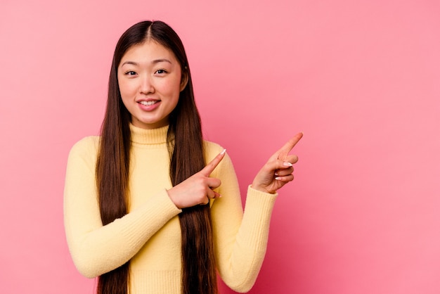 Young chinese woman isolated on pink wall shocked pointing with index fingers to a copy space.