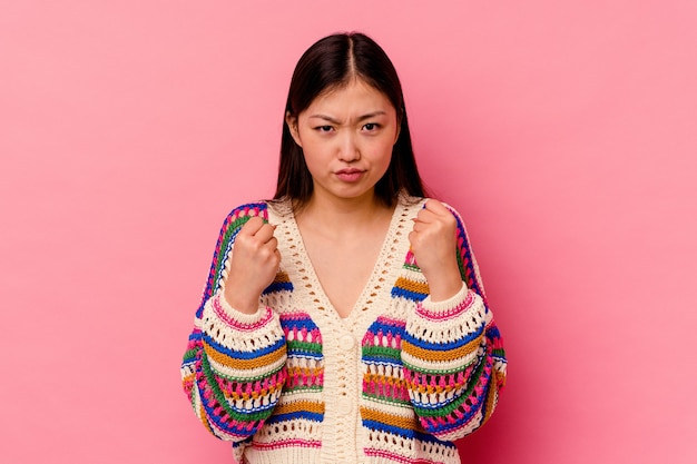 Young chinese woman isolated on pink wall showing fist, aggressive facial expression.