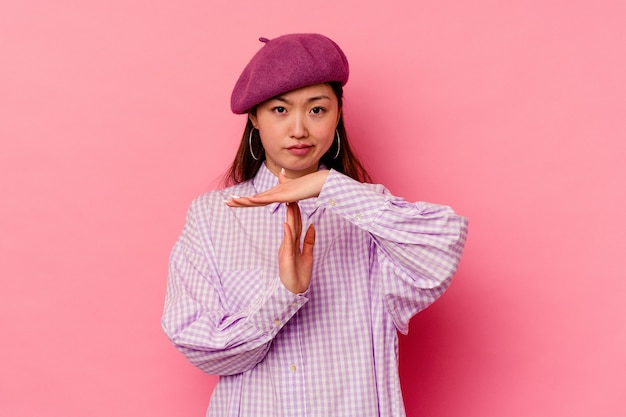 Young chinese woman isolated on pink wall showing a timeout gesture.