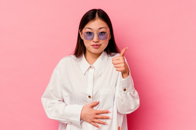 Young chinese woman isolated on pink wall touches tummy, smiles gently, eating and satisfaction concept.