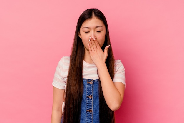 Young chinese woman isolated on pink wall yawning showing a tired gesture covering mouth with hand