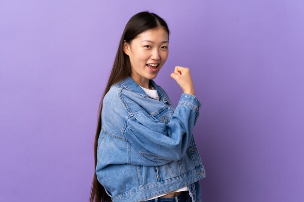 Молодая китайская женщина над изолированной фиолетовой стеной празднуя победу