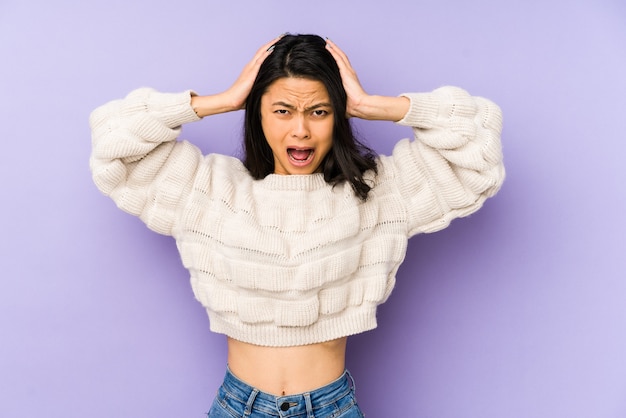 Young chinese woman isolated on a purple wall covering ears with hands trying not to hear too loud sound