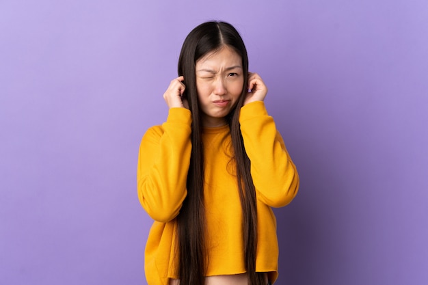 Young chinese woman over isolated purple wall frustrated and covering ears