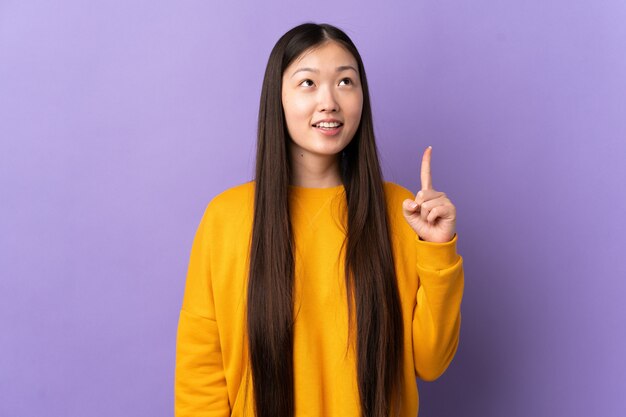 Young Chinese woman over isolated purple wall pointing up and surprised